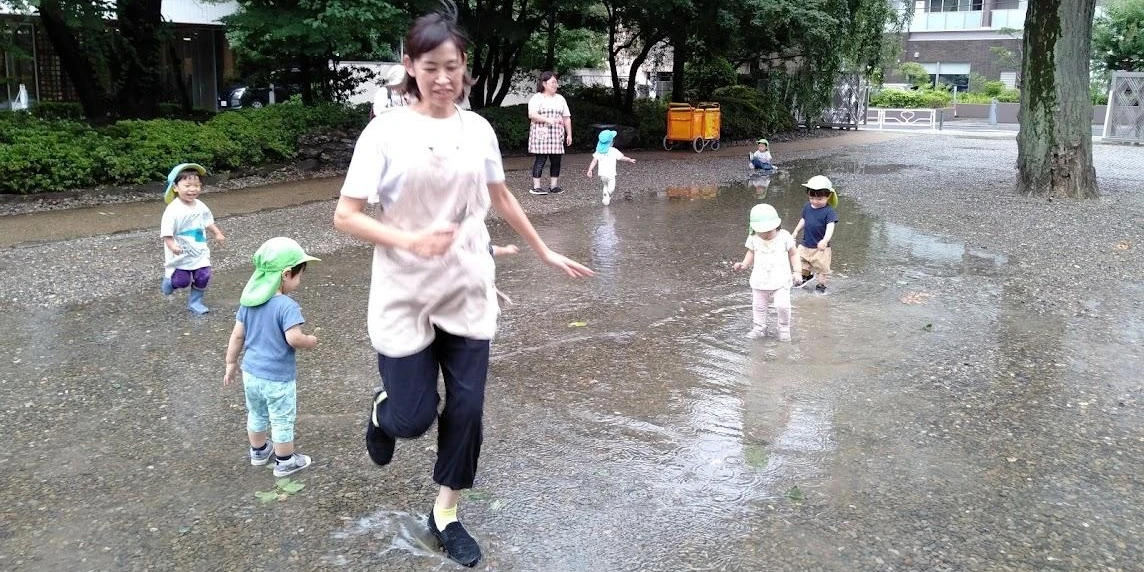 水たまりで遊ぶ保育士と子供たち