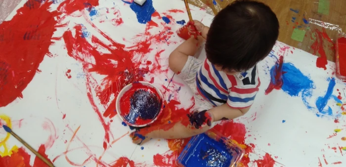 大きな紙で絵具遊びをする子供